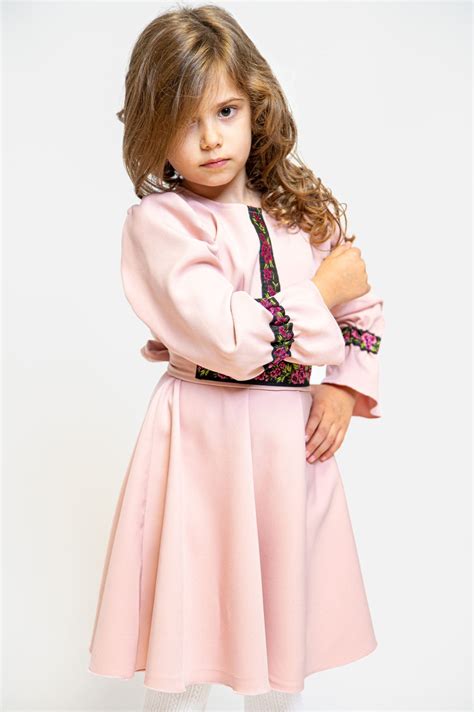 Fetiță îmbrăcată într-o rochiță elegantă de botez, zâmbind.