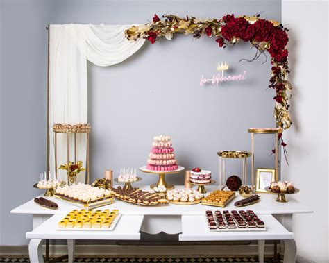 Exemplu de candy bar la un botez, cu o varietate de deserturi individuale, aranjate pe mai multe niveluri, într-o paletă de culori armonioasă.