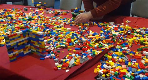 Copii și adulți construind diverse obiecte și personaje din piese LEGO, pe baza unor fișe de activități.