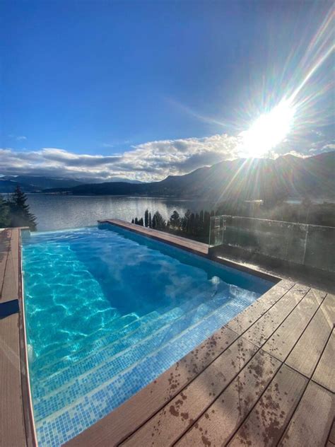 O piscină exterioară cu apă limpede, înconjurată de șezlonguri și vegetație, sub un cer senin.