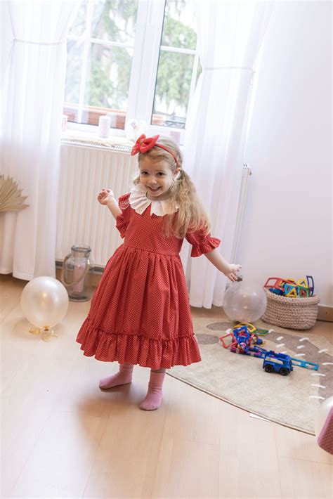 Fetiță într-o rochiță roșie de Crăciun, zâmbind lângă un brad împodobit