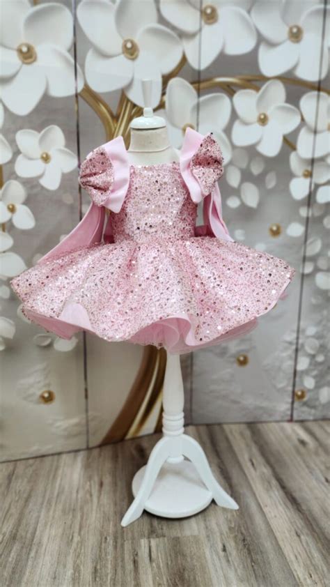 Două fetițe zâmbind, una purtând o rochiță roz cu paiete, cealaltă o rochiță albă cu bentită asortată