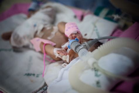 Copil în pat de spital, ținând de mână o persoană adultă (voluntar)