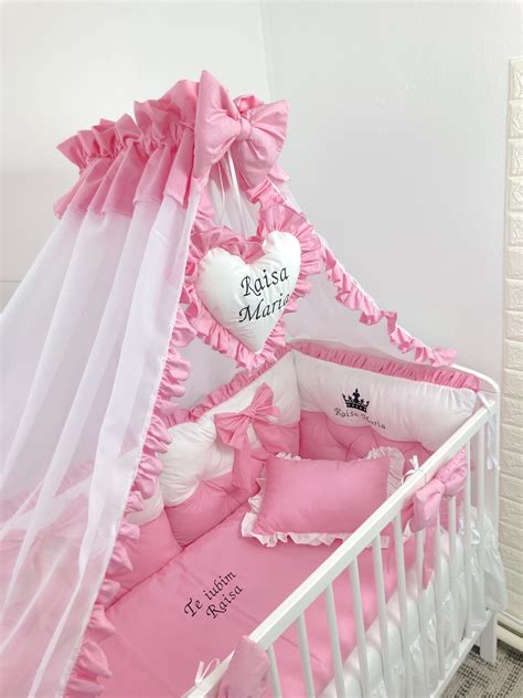 Ilustrație detaliată a componentelor setului de lenjerie pentru pătuț, evidențiind sistemul de prindere cu fundiță al protecțiilor și sistemul de închidere tip plic al husei de pilotă.