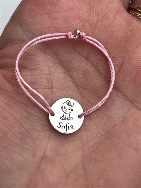 Fotografie: O brățară din aur pentru bebeluș, gravată cu nume și o inimioară, purtată pe mânuța unui copil