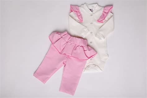 Fotografie cu un bebeluș îmbrăcat într-un costumaș format din body și pantalonași cu botosei.