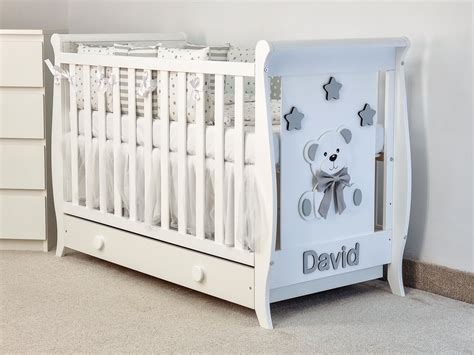 Ilustrație cu un patut de bebe din lemn cu tematică de ursuleț, decorat cu elemente vesele.