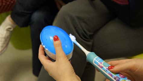 Diagramă pas cu pas care arată cum să fixezi periuța degetar pe deget și cum să aplici pasta de dinți.