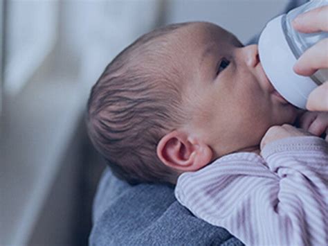 Parinte care hraneste bebelusul cu biberonul, intr-un ambient placut